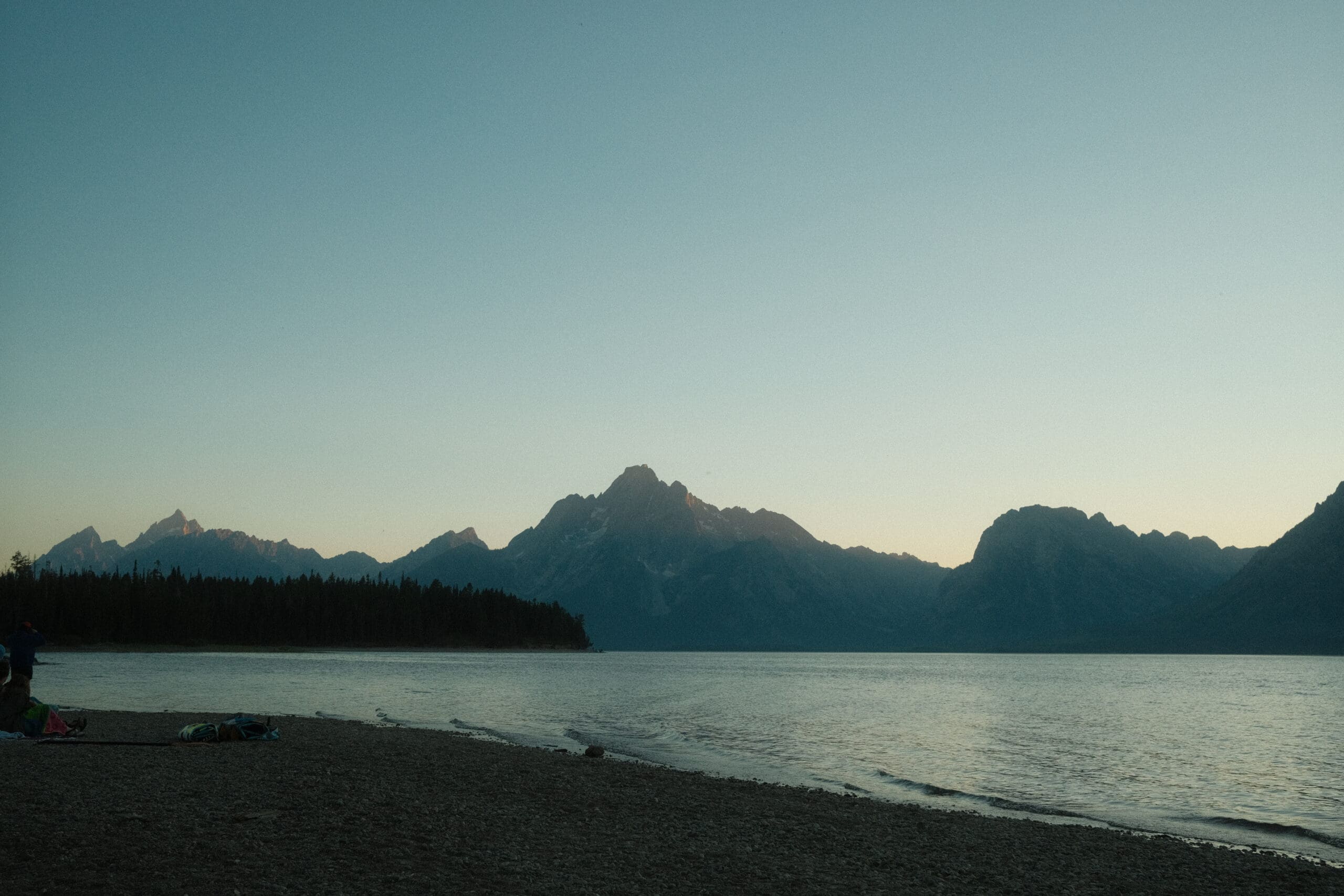 National Park Mountain range silhouetted at dusk above a calm lake shoreline in Wyoming.
