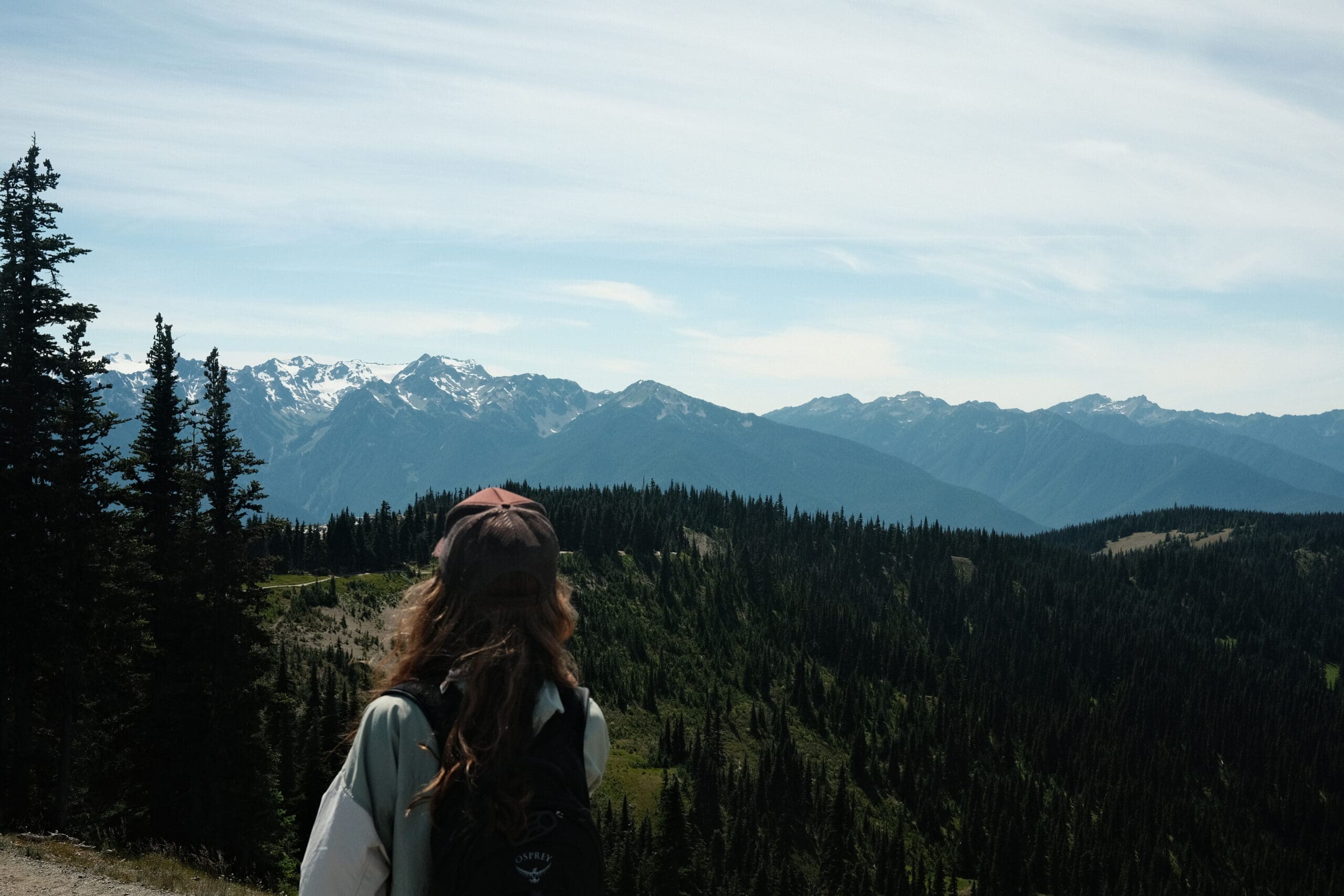 Hiker adjusting a packable shell jacket on a mountain trail with changing cloud cover above